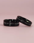 Two black rings with speckled patterns on a pink background