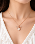 A close-up of a woman wearing a delicate rose gold chain necklace with a fairy pendant featuring a white pearl center.