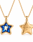 Two gold star-shaped pendant necklaces on a white background, showing the front and back. The front pendant features a sparkling blue enamel background with a white tooth in the center.