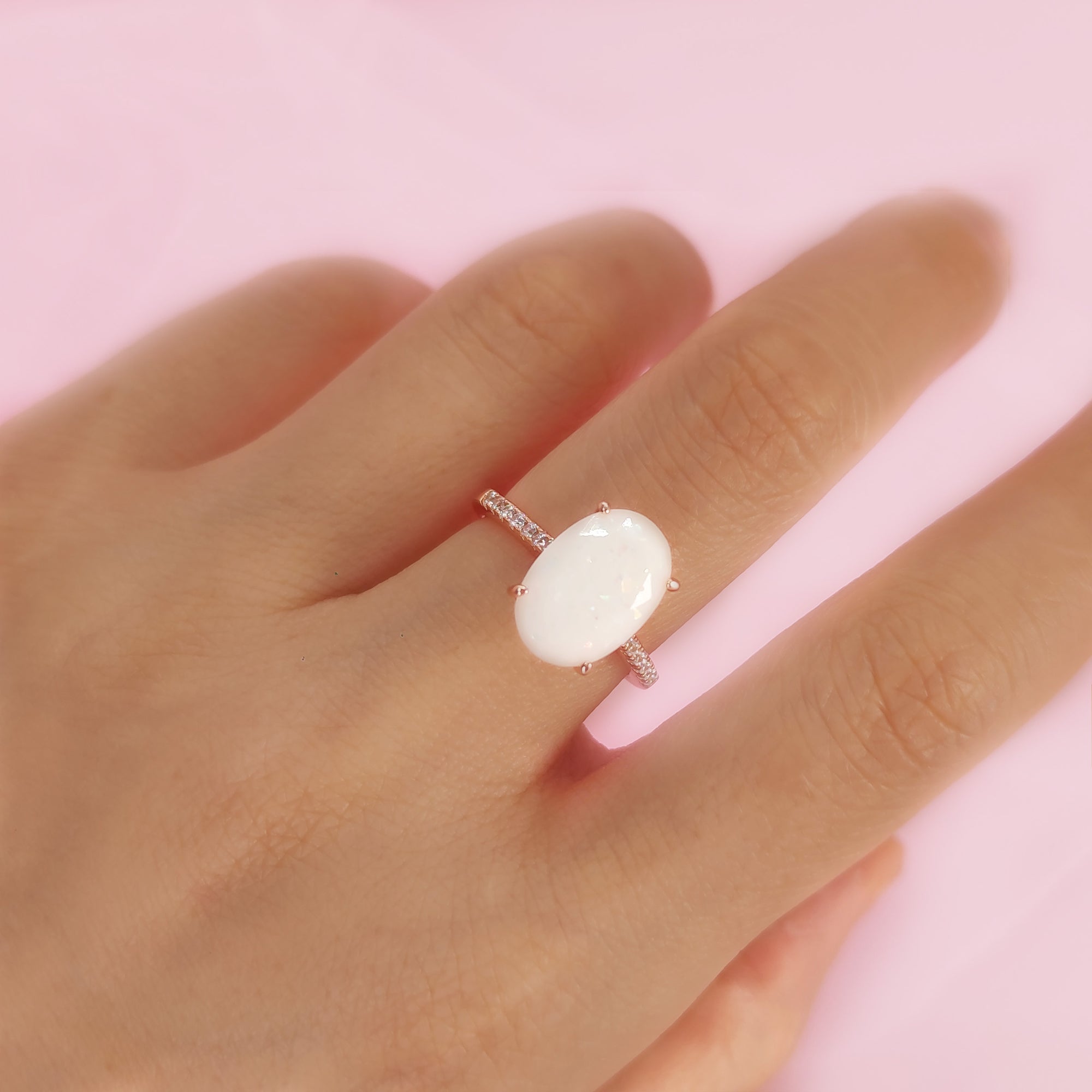Ring with a large white stone on a hand against a pink background