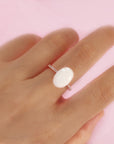 Ring with a large white stone on a hand against a pink background