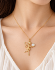 A close-up of a woman wearing a delicate gold chain necklace with a fairy pendant holding a small ball with baby tooth, styled with a white top.