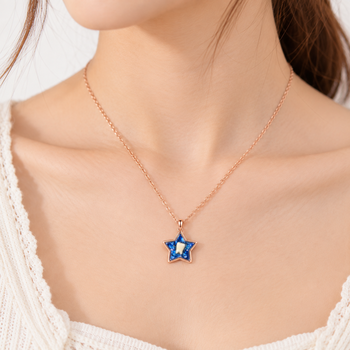 A close-up of a model wearing a delicate rose gold chain necklace with a star-shaped pendant. The pendant features a deep blue outer border and a white center stone.