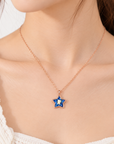 A close-up of a model wearing a delicate rose gold chain necklace with a star-shaped pendant. The pendant features a deep blue outer border and a white center stone.