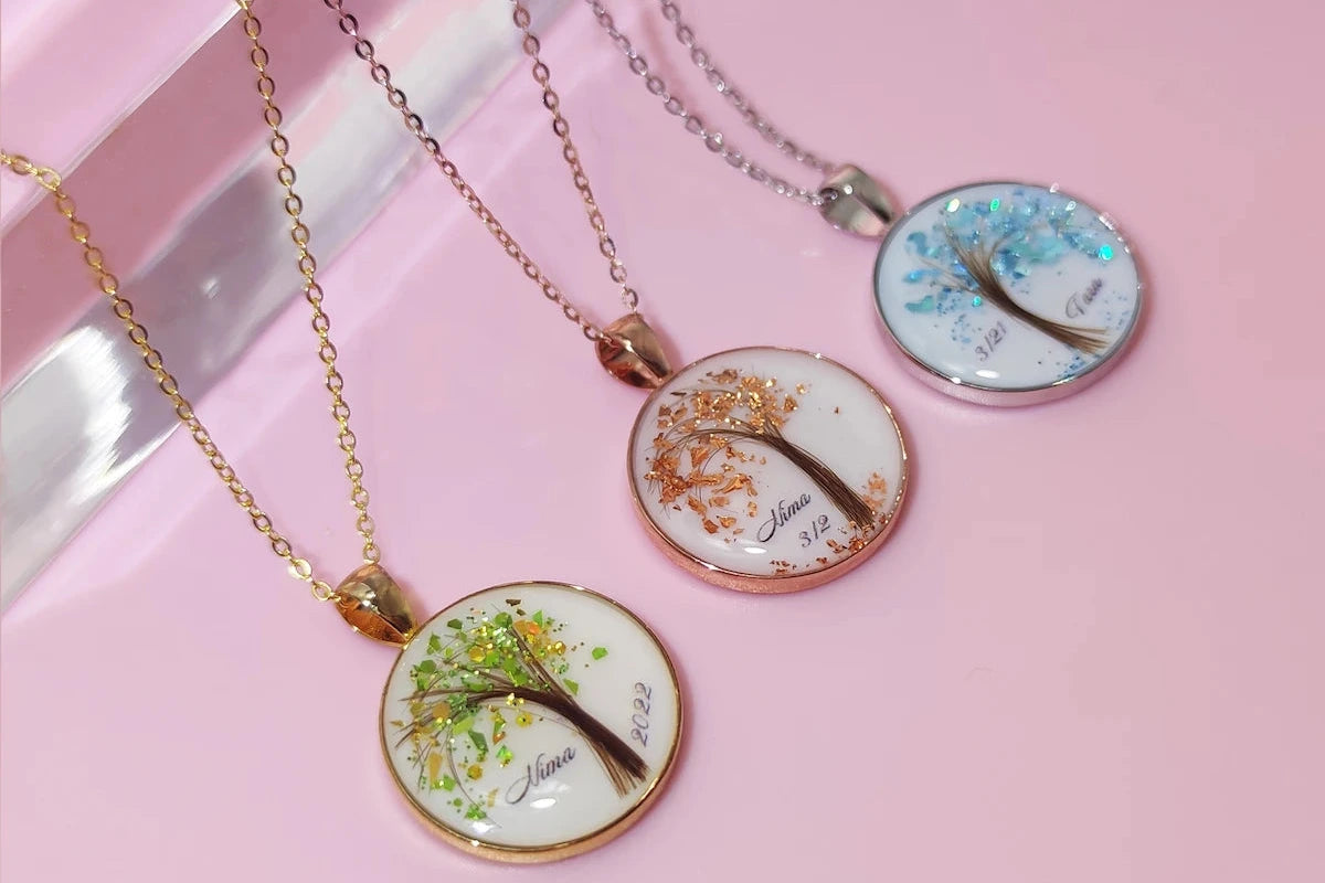 Three necklaces with tree-themed breastmilk pendants on a pink surface
