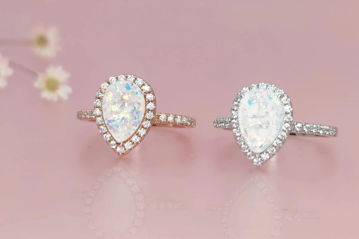 Three oval-shaped cremation gemstone rings on a pink background
