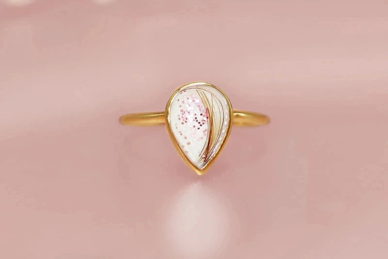 Gold ring with a teardrop-shaped  hair/fur gemstone on a soft pink background