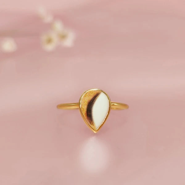 Gold hair/fur ring with a white stone on a pink background