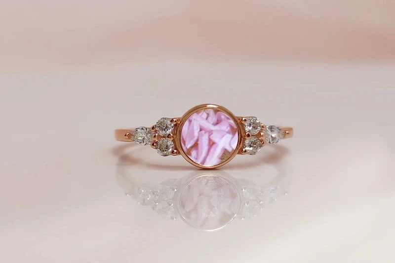 Rose gold ring with a pink pregnancy test cap gemstone on a reflective surface